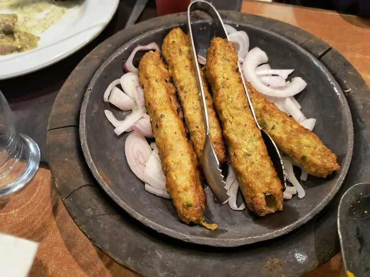 Seekh kababs on a sizzler plate with sliced onions